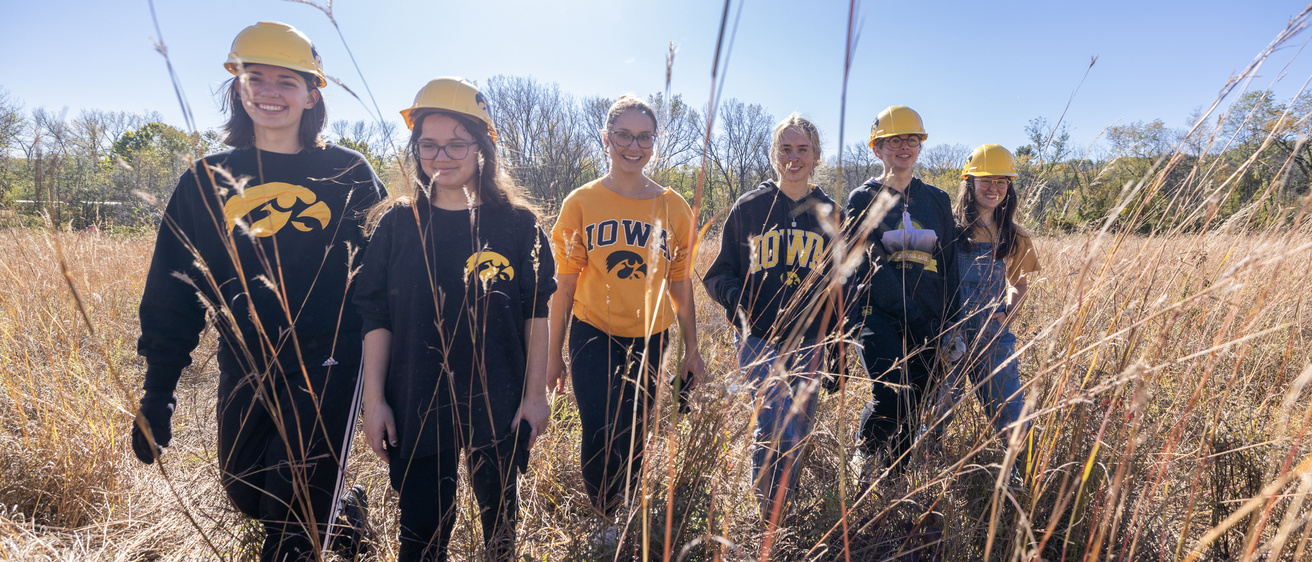 6 Iowa students wearing hawkeye hard hatswalking in a prairie doing field work